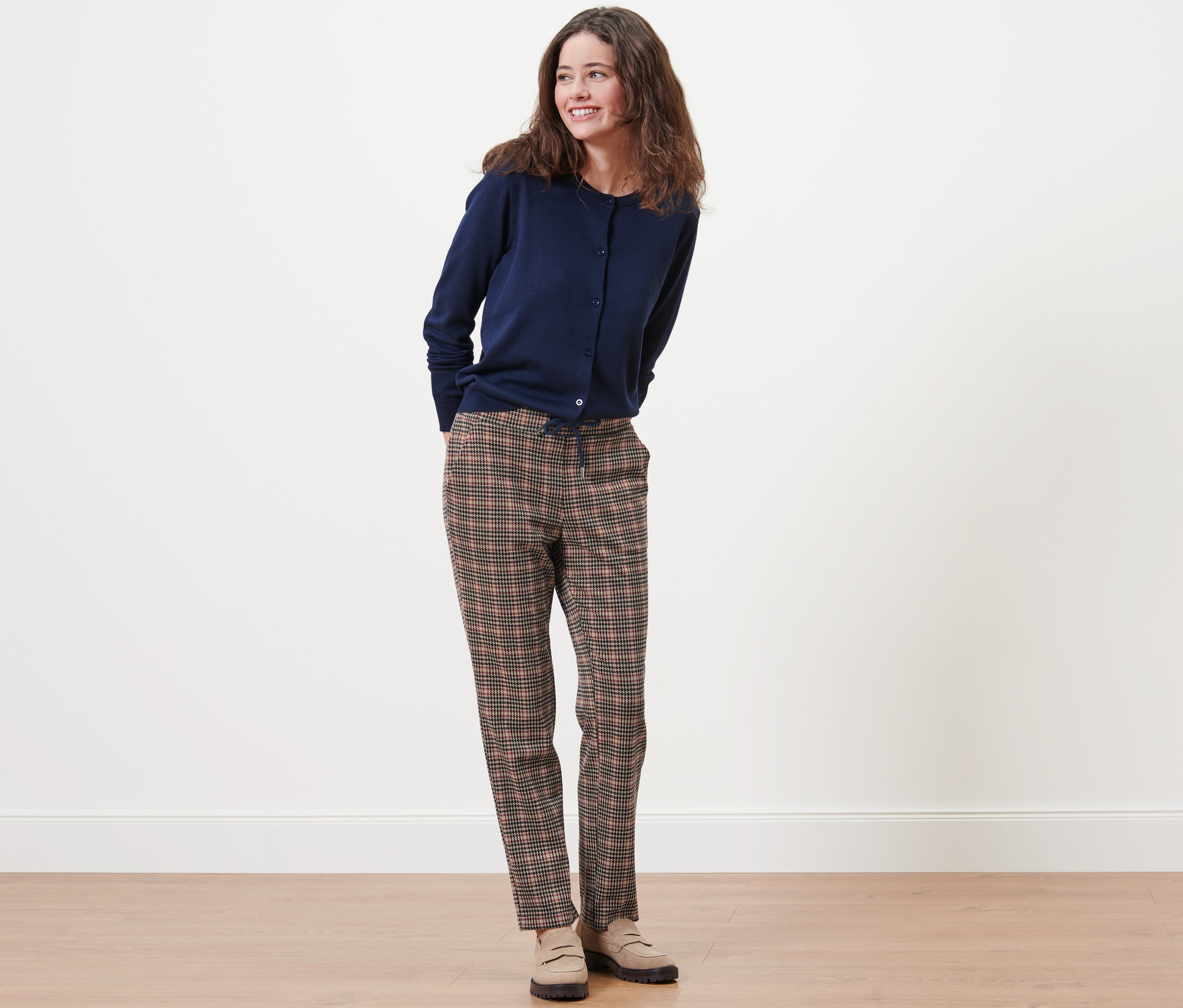 Eine Frau steht und trägt eine marineblaue Strickjacke und eine Joggpants mit Hahnentritt-Dessin.