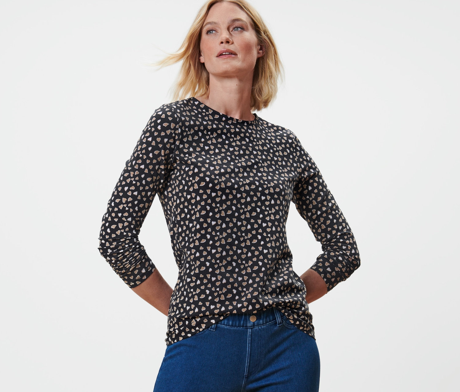 Blonde Frau posiert in einem Langarmshirt mit Alloverprint und blauen Jeans.