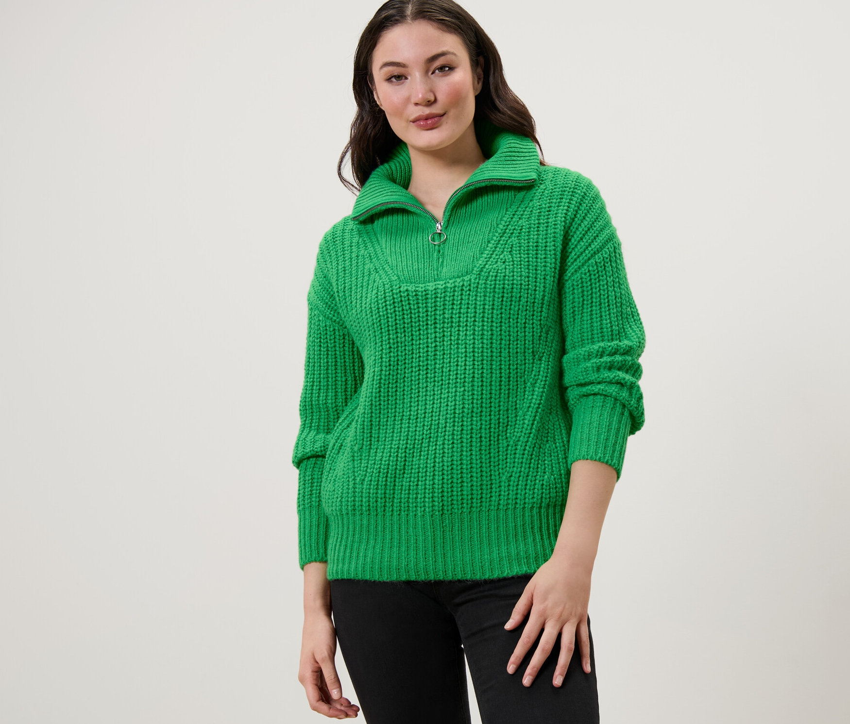 Frau trägt einen grünen Grobstrick-Troyer und schwarze Jeans.