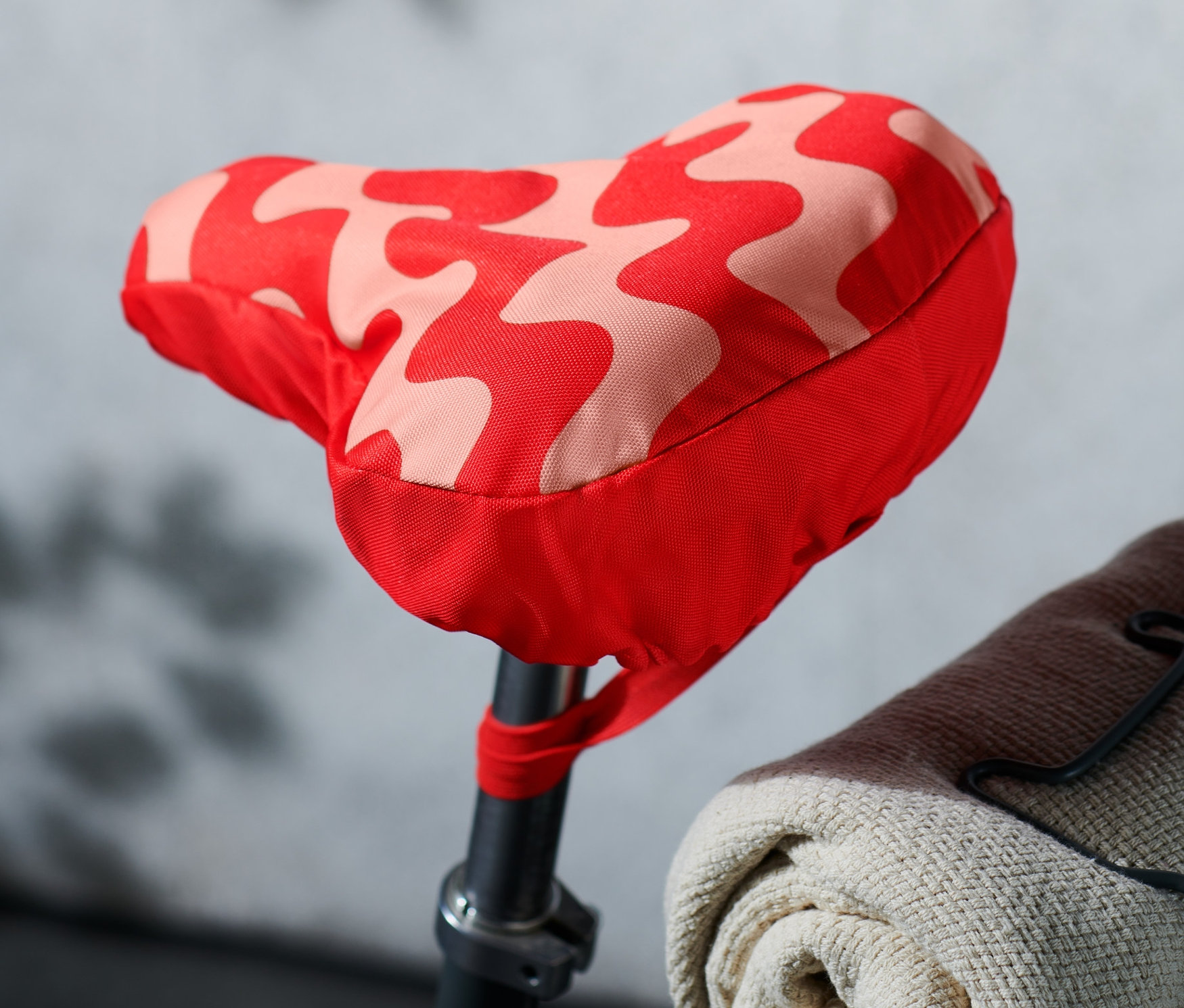 Detailaufnahme eines Fahrradsattels mit einem rot-rosa gemusterten Fahrradsattelbezug.