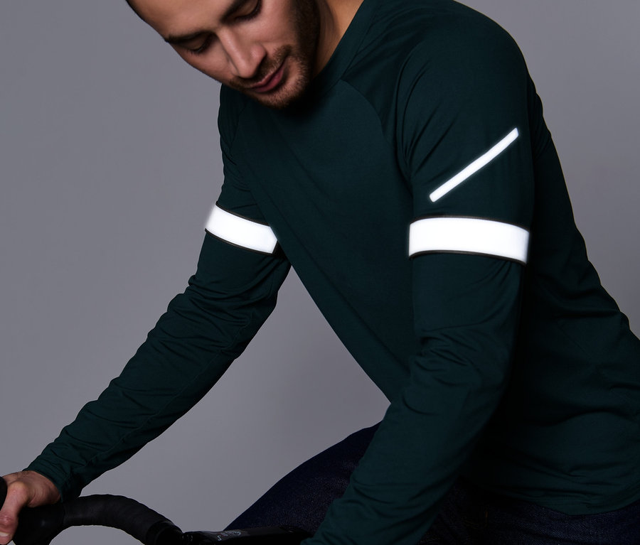 Mann im grünen Langarmshirt hält einen Fahrradlenker. An den Hosen sind 2 Reflektor-Hosenbänder befestigt.