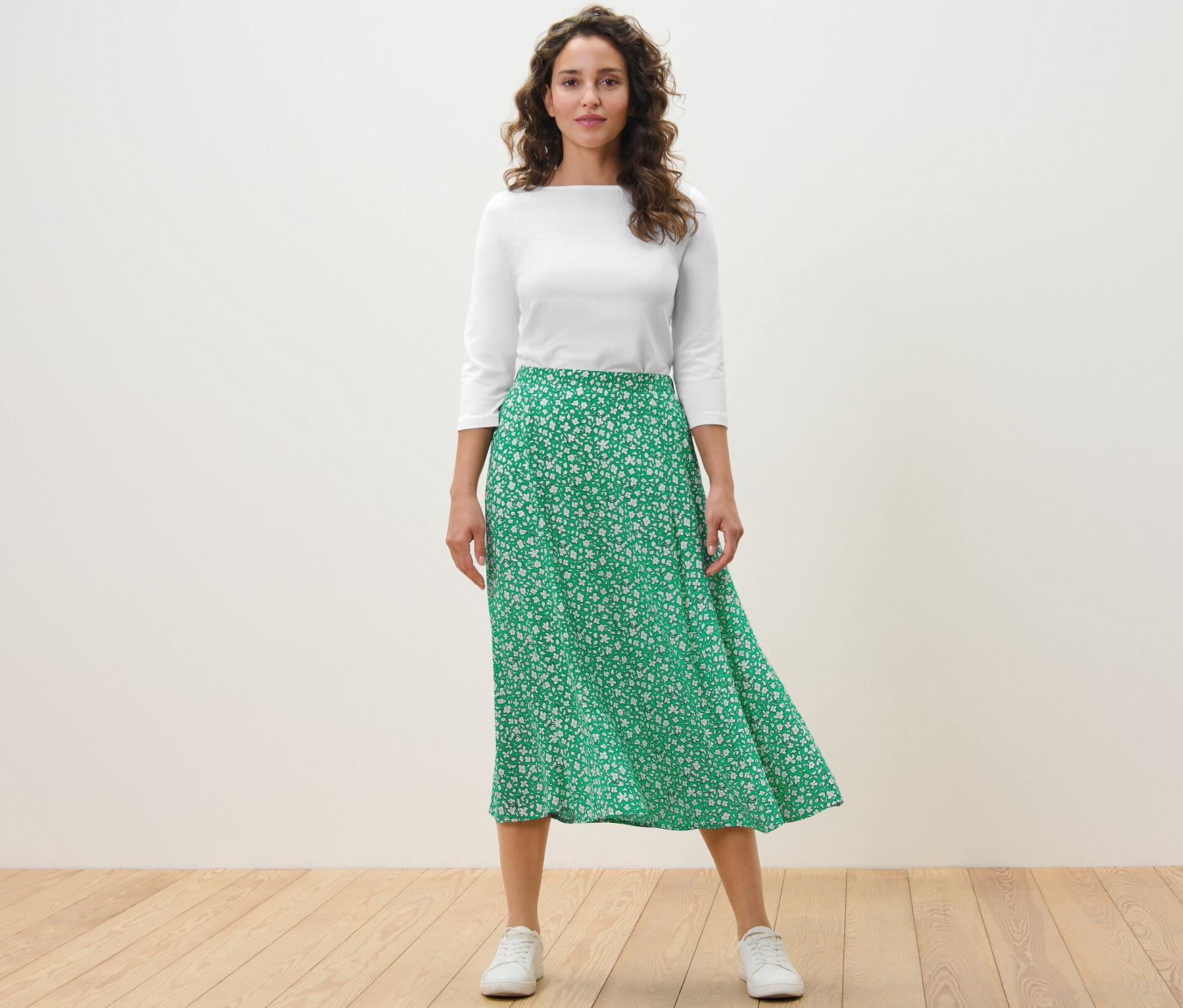 Frau steht und trägt einen bedruckten Midirock, grün.