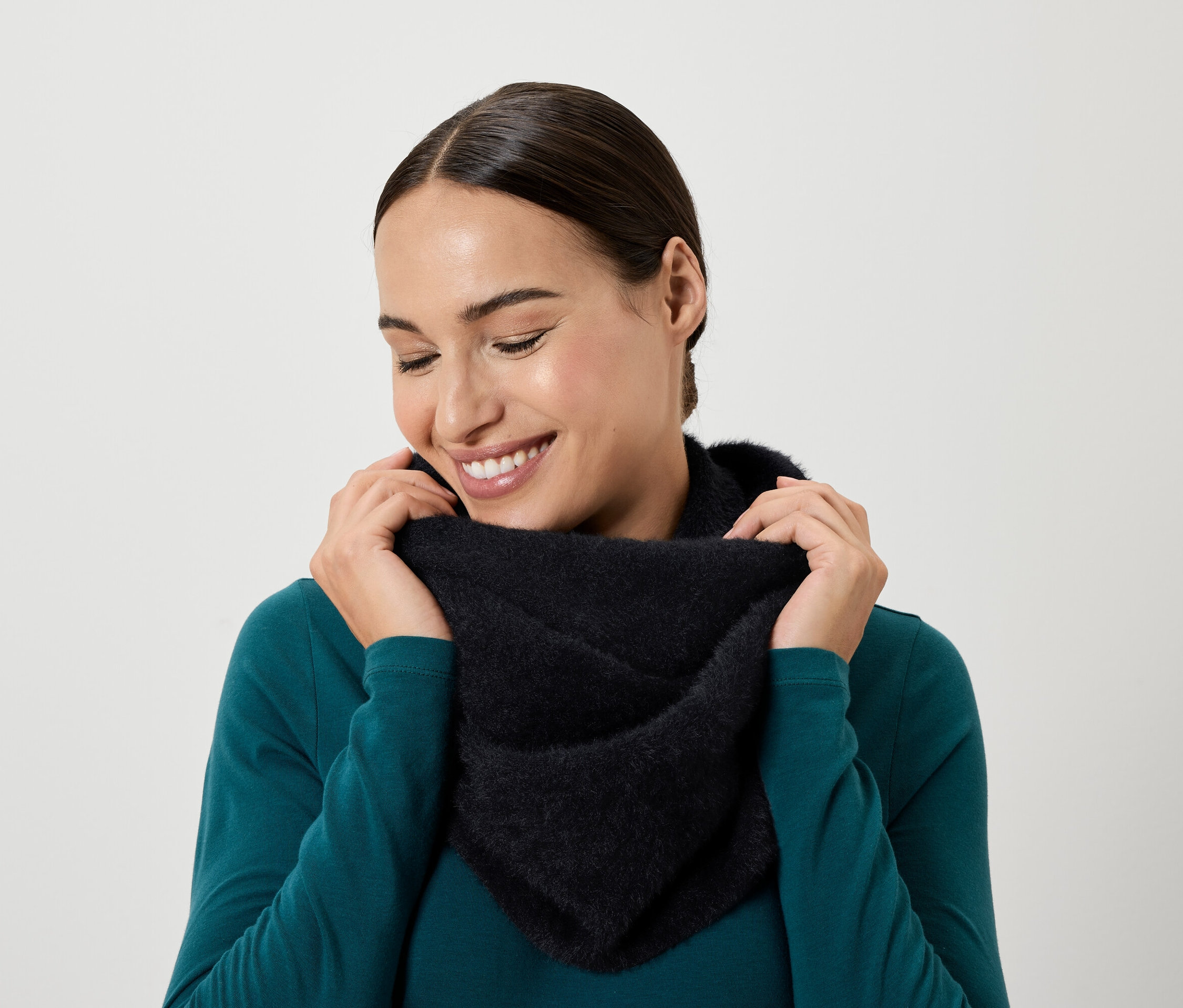 Lächelnde Frau blickt nach unten und hält mit ihren Händen einen schwarzen Schal um ihren Hals.