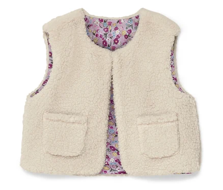 Eine ärmellose, flauschige, cremefarbene Weste mit zwei aufgesetzten Taschen und einem floralen Innenfutter.