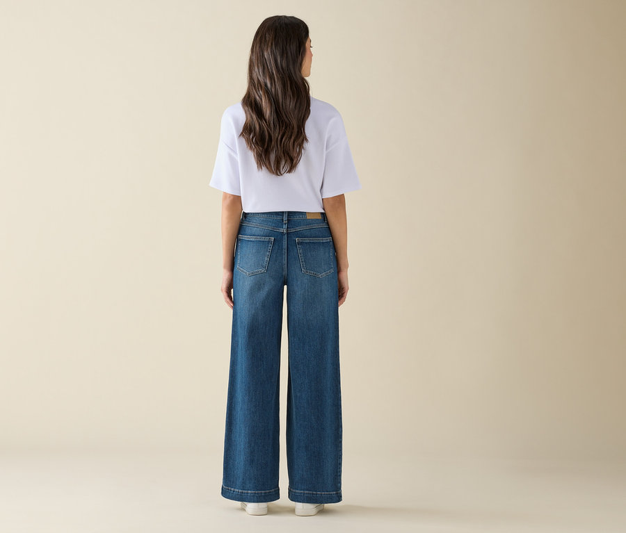 Frau steht mit dem Rücken zur Kamera und trägt weite Jeans und ein weißes T-Shirt.