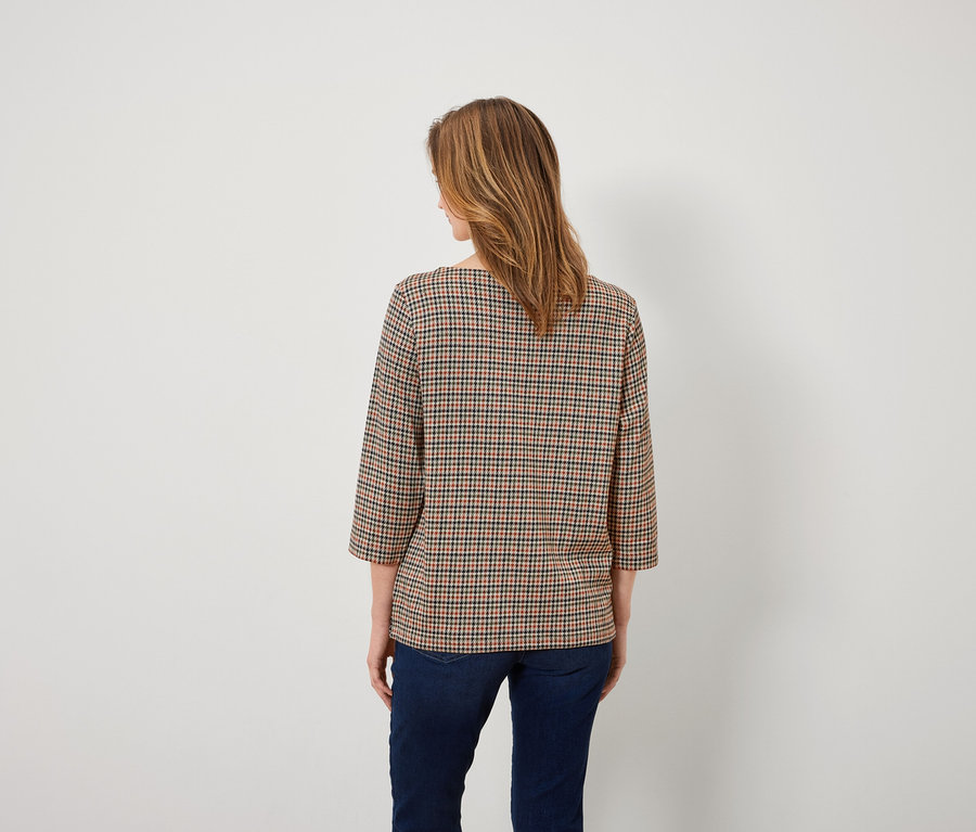 Frau mit dem Rücken zur Kamera trägt eine karierte Bluse und Jeans.