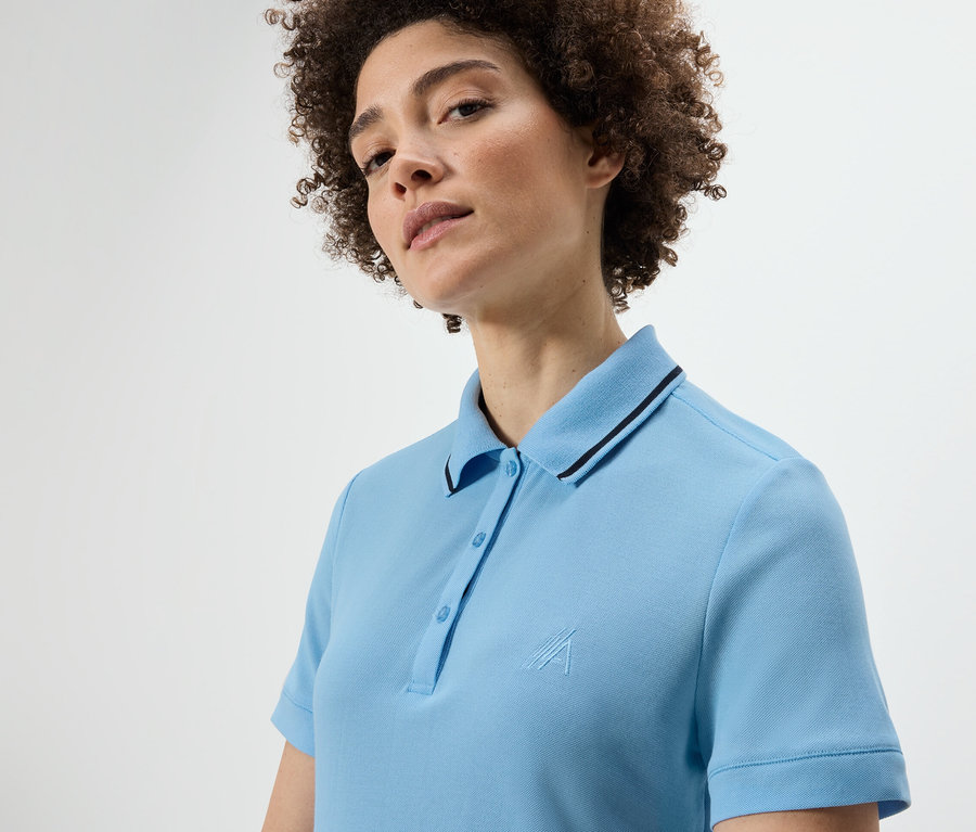 Frau mit lockigem Haar trägt ein hellblaues Funktionspoloshirt.