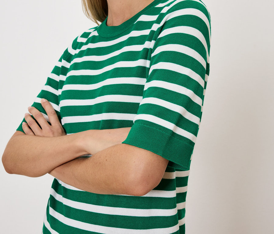 Frau mit verschränkten Armen trägt ein grün-weiß gestreiftes T-Shirt.