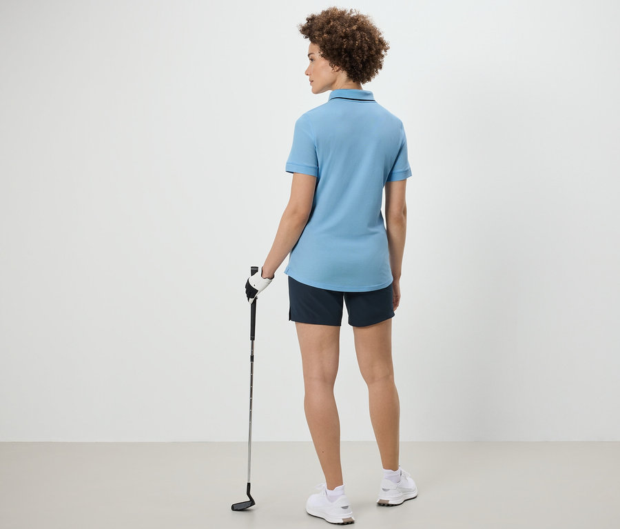 Frau von hinten hält einen Golfschläger und trägt ein hellblaues Funktionspoloshirt.