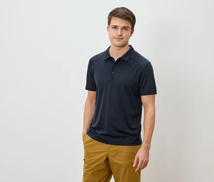 Mann mit marineblauem Poloshirt und goldbraunen Hosen, eine Hand in der Hosentasche.