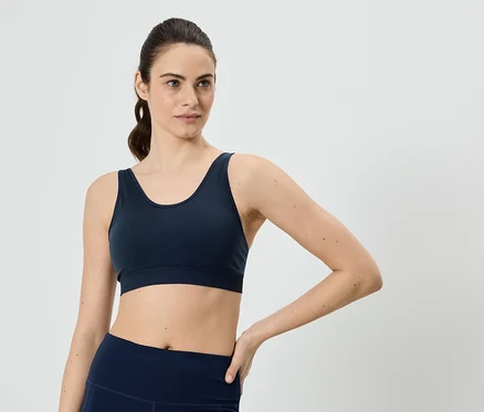 Frau mit Pferdeschwanz, die einen marineblauen Sport-BH und Leggings trägt und ihre Hand auf ihre Hüfte legt.