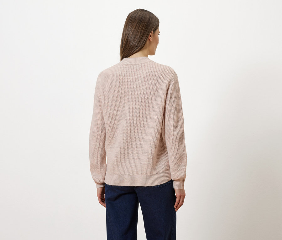 Frau von hinten in rosa Strickjacke und Jeans vor weißem Hintergrund.