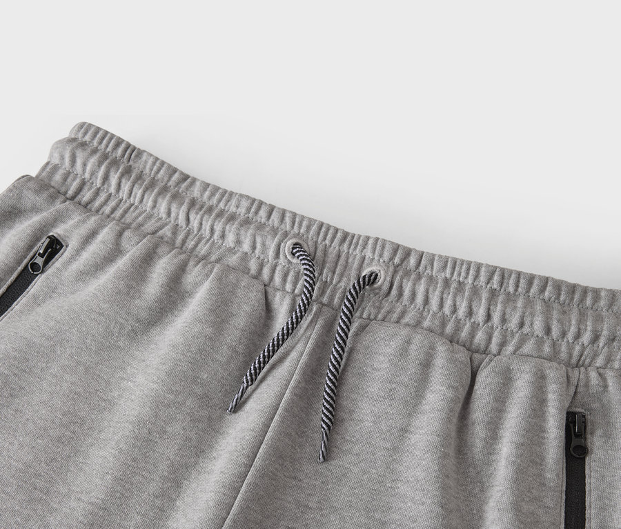 Nahaufnahme der Taille einer grauen Trainingshose mit Kordelzug und Reißverschlusstaschen.