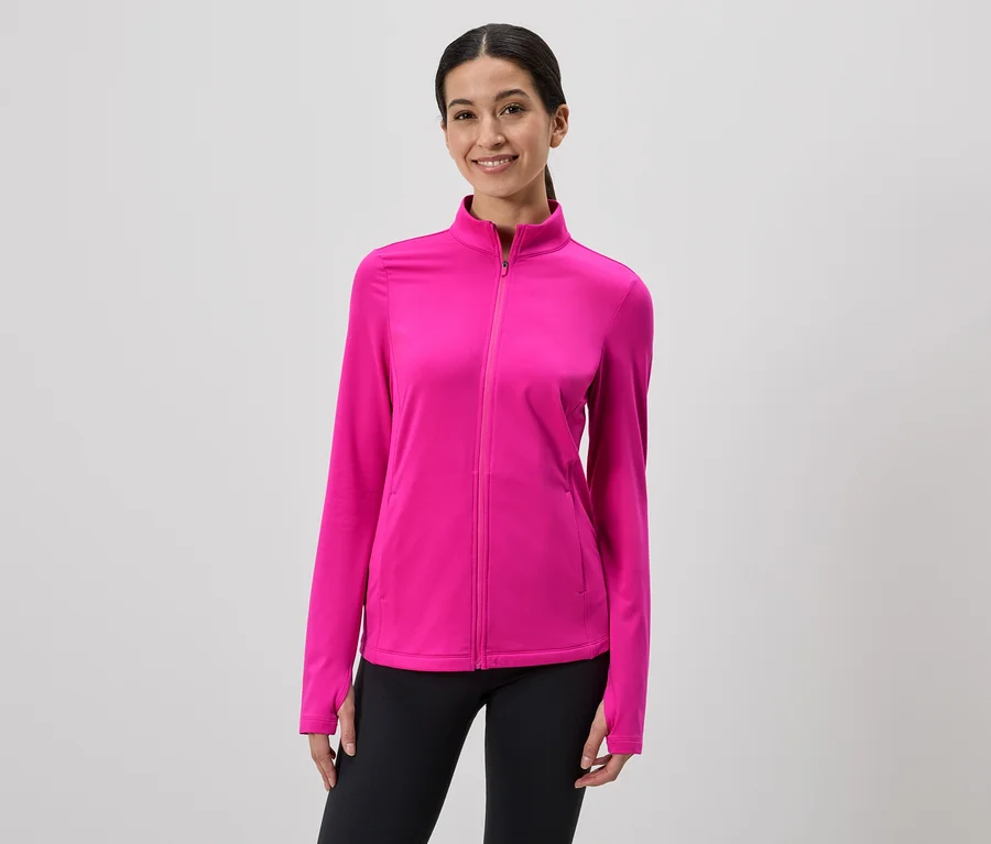 Frau mit Pferdeschwanz trägt pinke Jacke mit Reißverschluss und schwarze Leggings vor grauem Hintergrund.