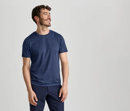 Ein Mann in einem blauen T-Shirt und einer dunkelblauen Hose lächelt und blickt nach rechts.