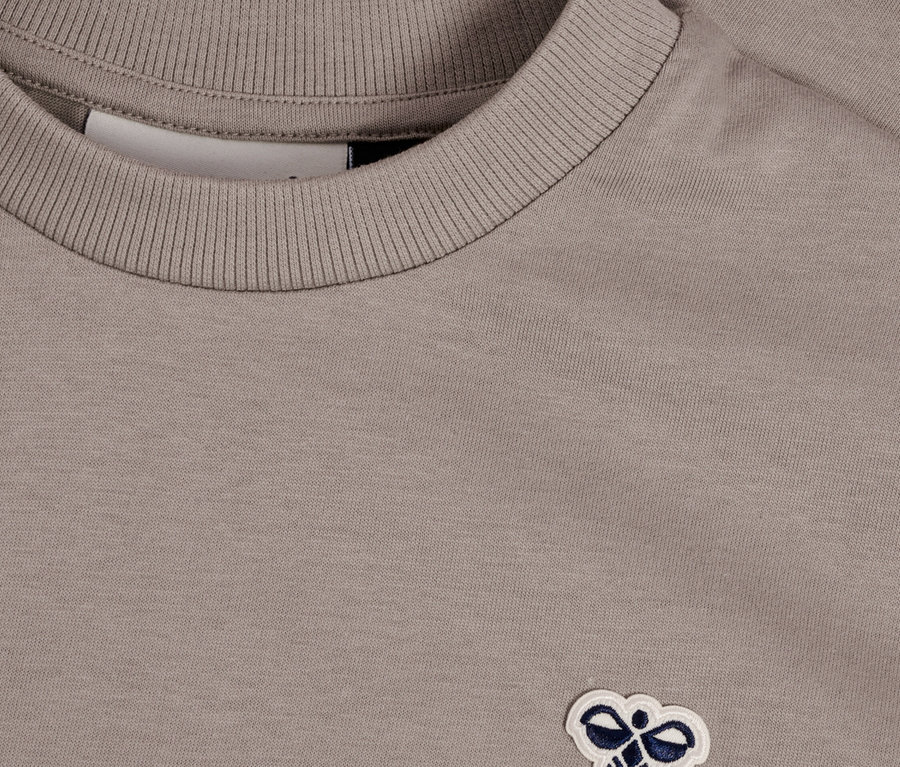 Nahaufnahme eines grauen T-Shirts mit einem kleinen, gestickten Logo.