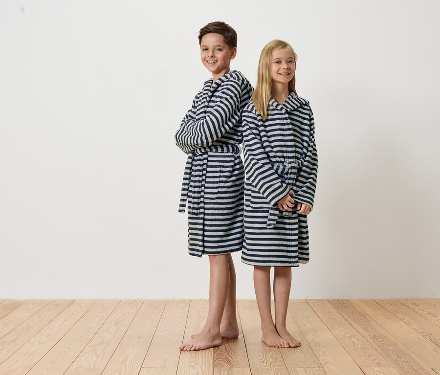 Ein Junge und ein Mädchen stehen Rücken an Rücken und tragen gestreifte Bademäntel.