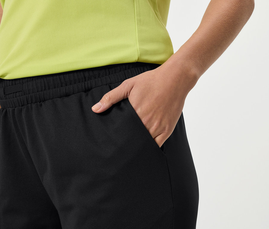 Nahaufnahme einer Person, die schwarze Jogginghose und ein gelbes Oberteil trägt und ihre Hand in die Hosentasche steckt.