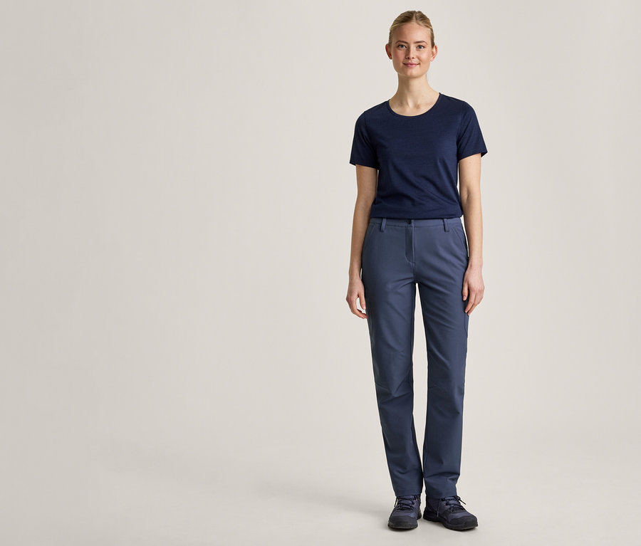 Eine junge Frau steht frontal vor einem hellen Hintergrund, trägt ein dunkelblaues T-Shirt, eine blaue Hose und dunkelblaue Schuhe.