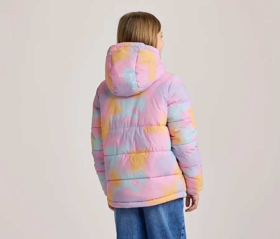 Person von hinten in einer bunten, wattierten Jacke mit Kapuze und Batikmuster in Rosa, Lila, Gelb und Blau, dazu blaue Jeans.