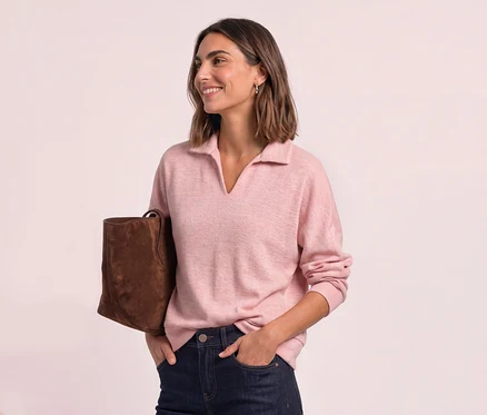 Lächelnde Frau mit kurzem Haar, die ein rosafarbenes Street One Poloshirt, dunkle Jeans und eine braune Tasche trägt.