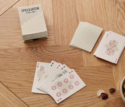 Auf einem Holztisch liegen ein Spielkarten-Set »Skat«, ein Wasserglas und eine Schale mit Nüssen.