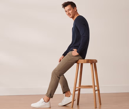 Mann sitzt auf einem Holzhocker und trägt eine sandfarbene Chino.