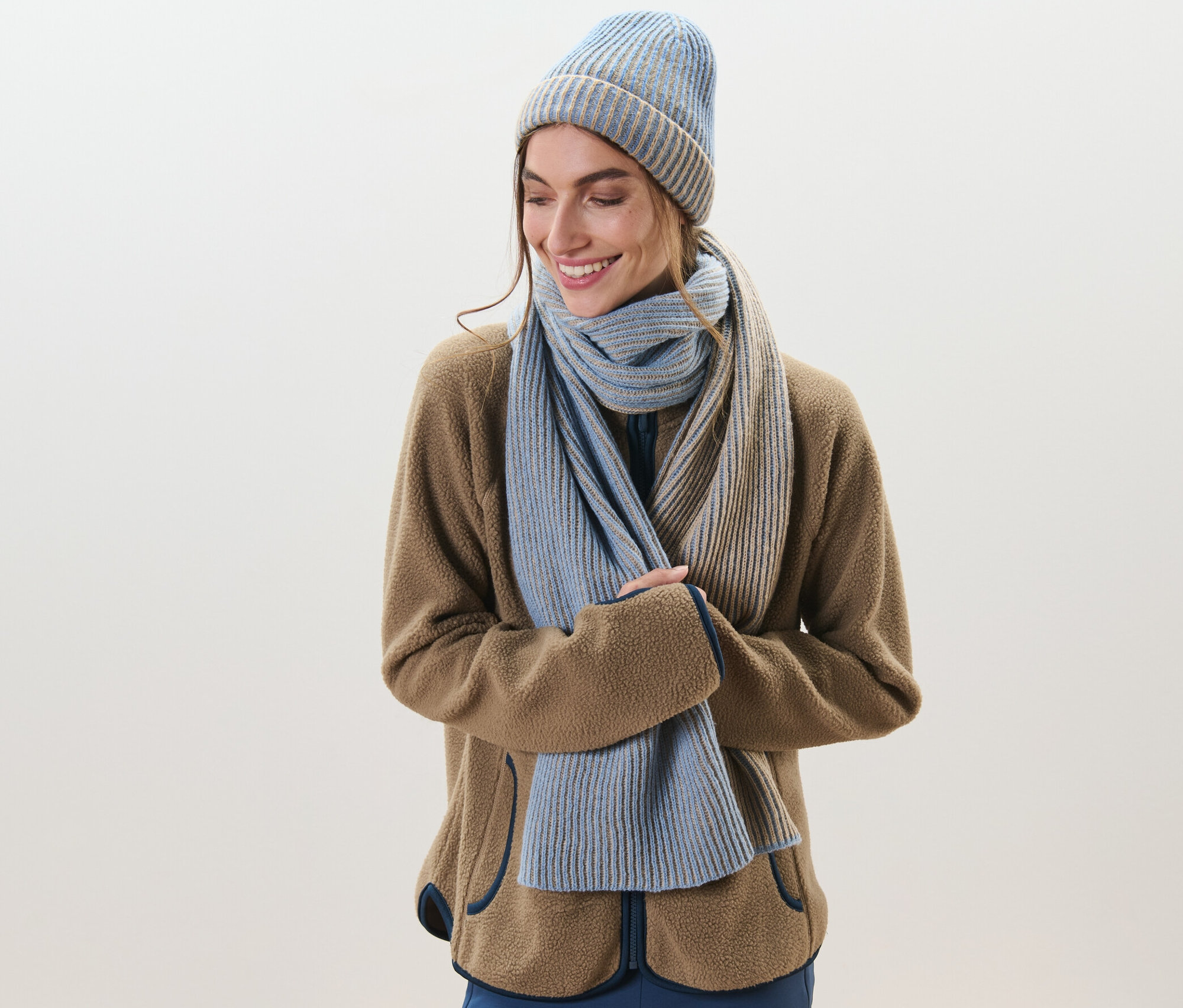 Frau lächelt und trägt einen Strickschal und eine Mütze.