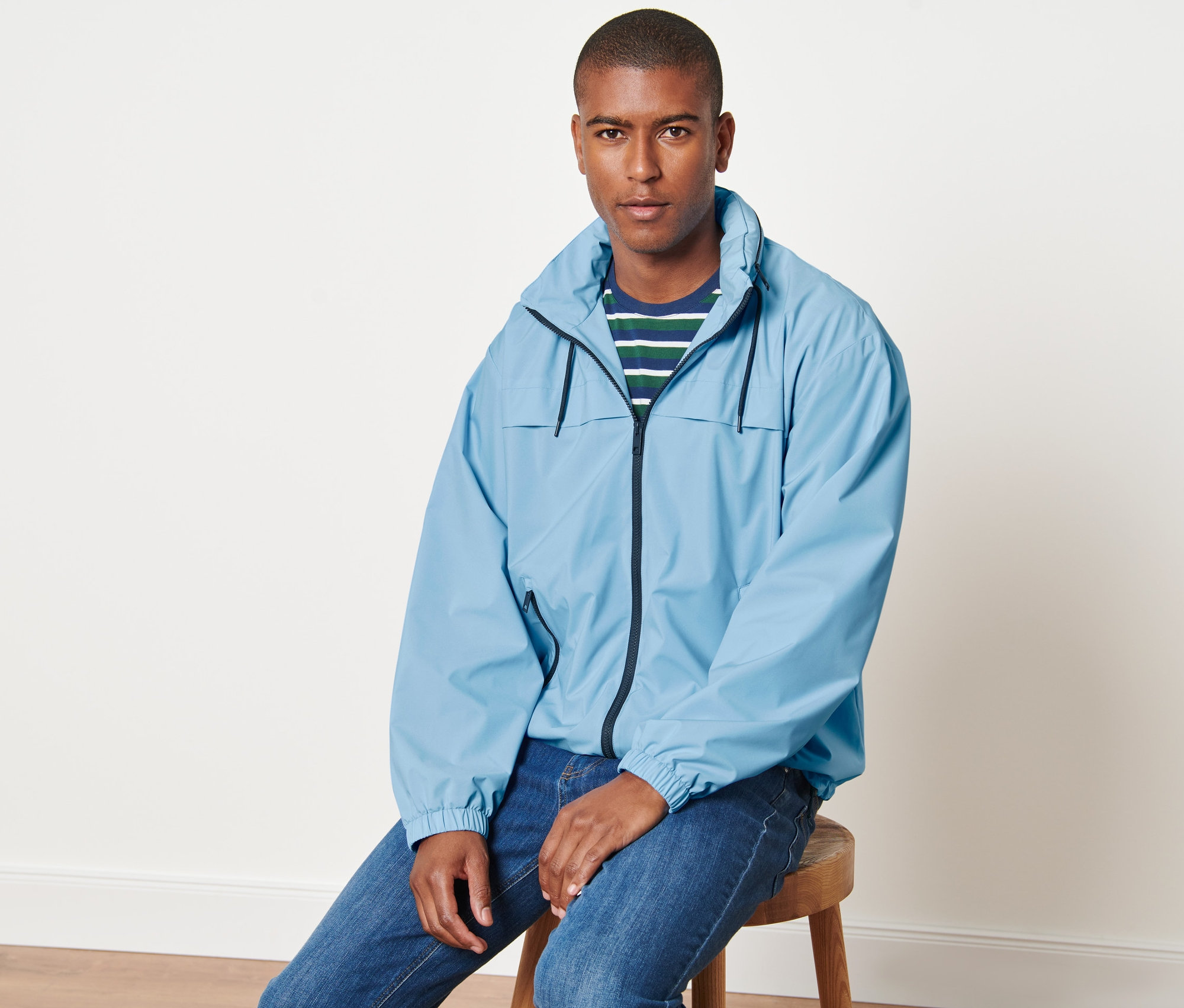 Mann sitzt auf einem Hocker und trägt eine hellblaue Windbreaker-Jacke.