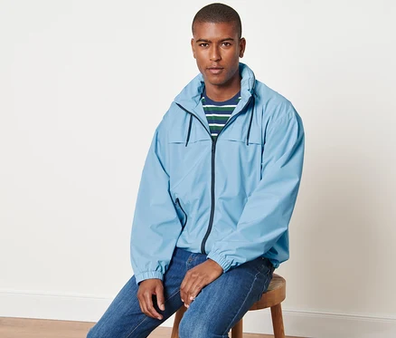 Mann sitzt auf einem Hocker und trägt eine hellblaue Windbreaker-Jacke.