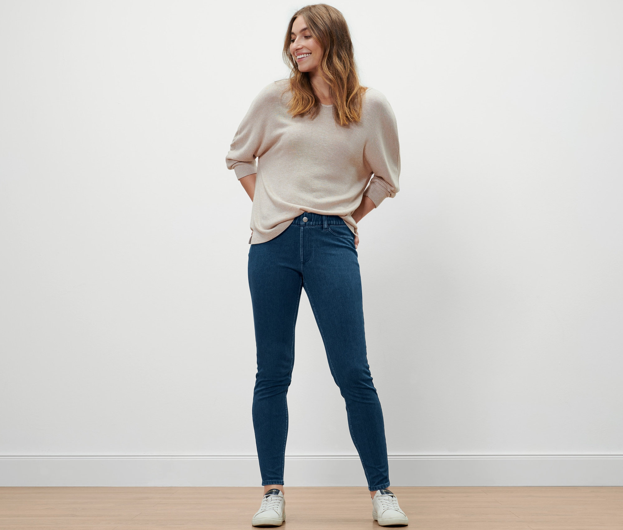 Frau posiert in Jeggings, Pullover und Turnschuhen.