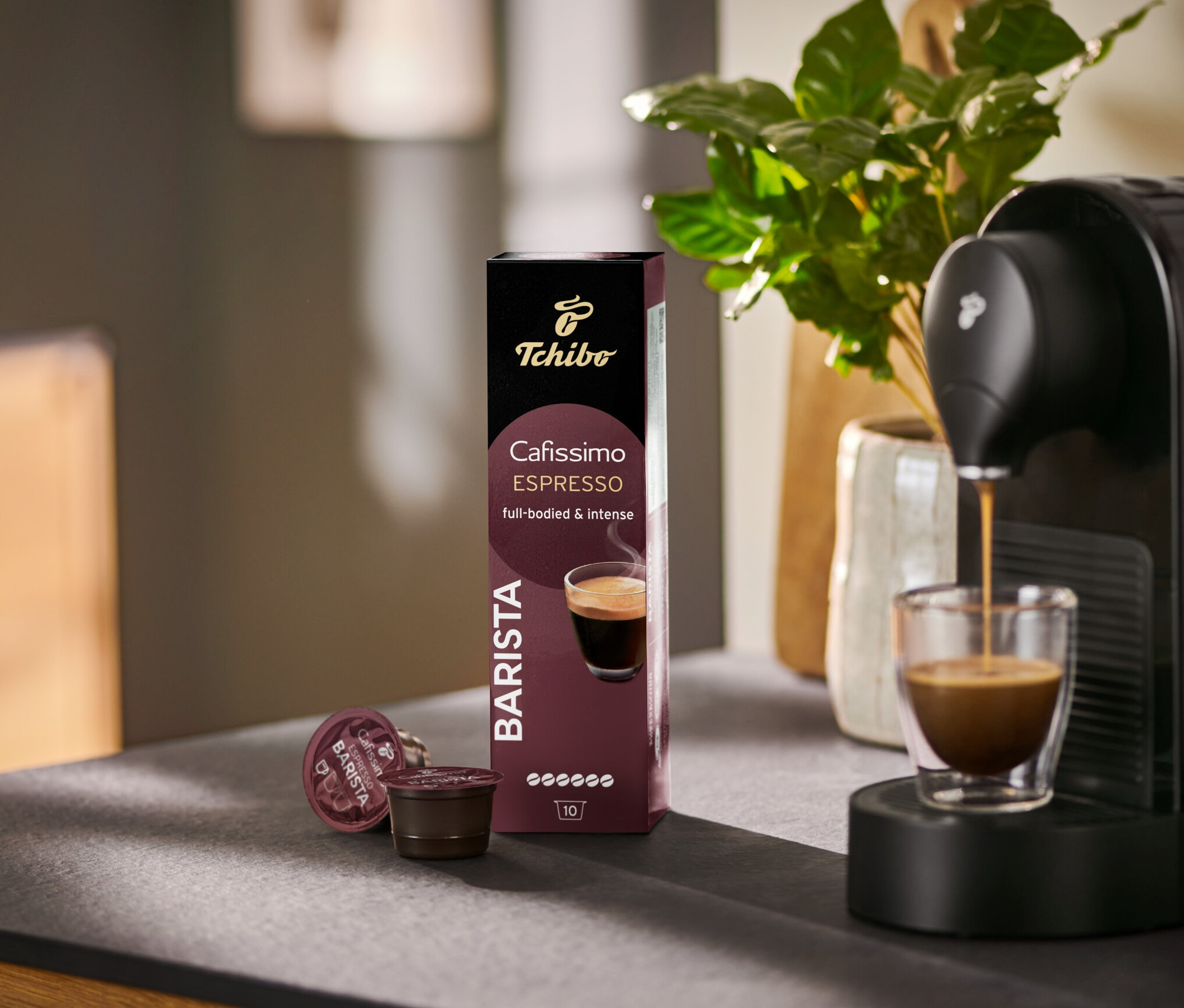 Espresso läuft aus einer Cafissimo BARISTA Maschine in ein Glas, daneben eine Packung mit 10 Kapseln.