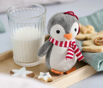 Ein Plüschpinguin mit Schal steht neben einem Glas Milch und Keksen auf einem Holztablett.