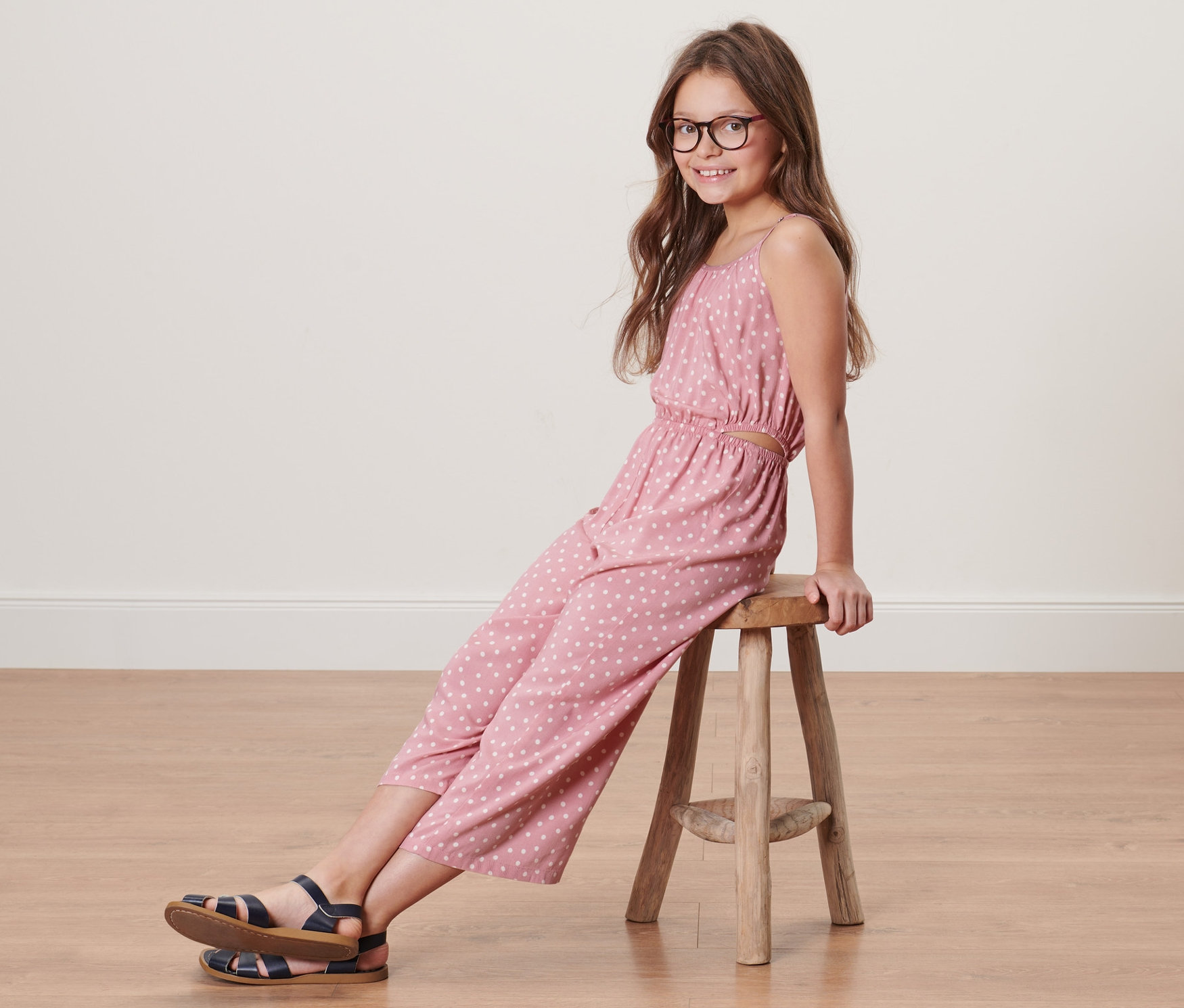 Mädchen sitzt auf einem Hocker und trägt einen Kinder-Web-Jumpsuit in 7/8-Länge.