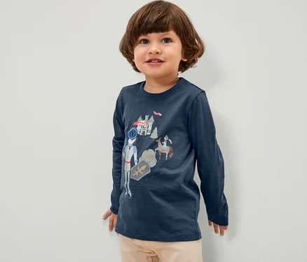 Junge trägt ein blaues Langarmshirt mit Ritter-Motiv.