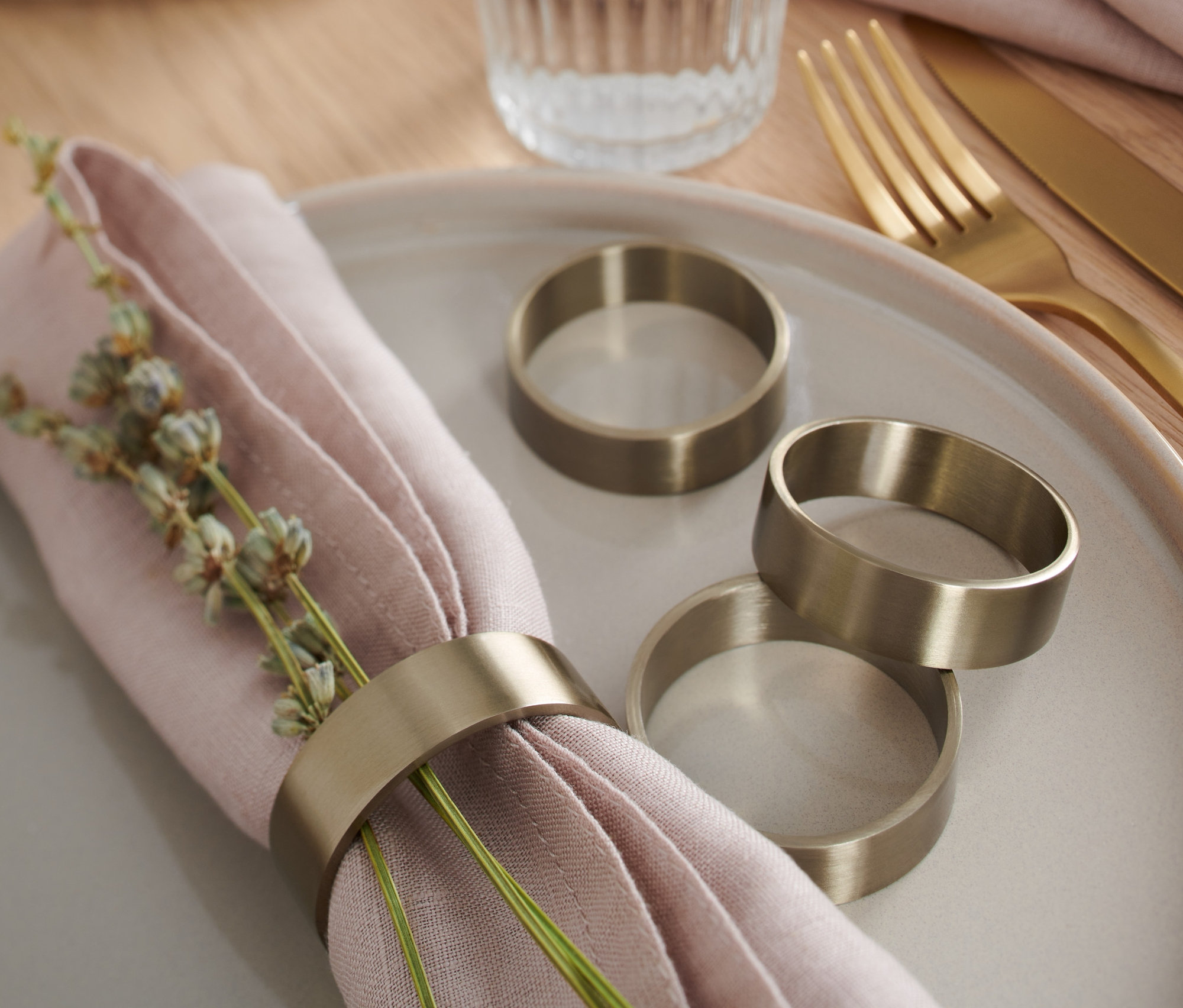 Auf einem Teller liegen eine rosa Serviette mit Dekoration und 4 Serviettenringe. Drei Serviettenringe liegen daneben.