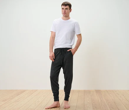 Mann steht in weißem T-Shirt und Feinstrick-Homewearhose.