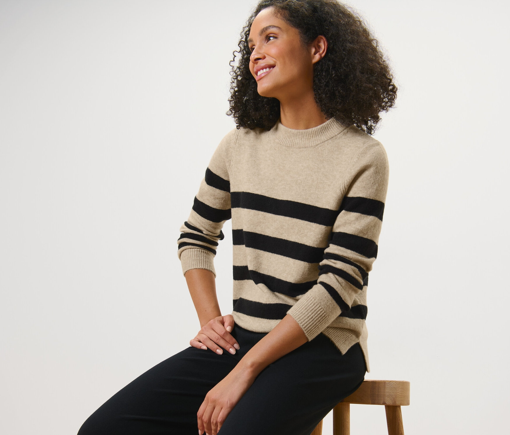 Frau sitzt auf einem Hocker und trägt einen gestreiften Strickpullover.