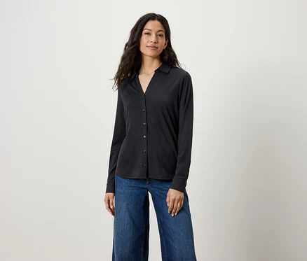 Eine Frau trägt ein schwarzes Langarmhemd und blaue Jeans.