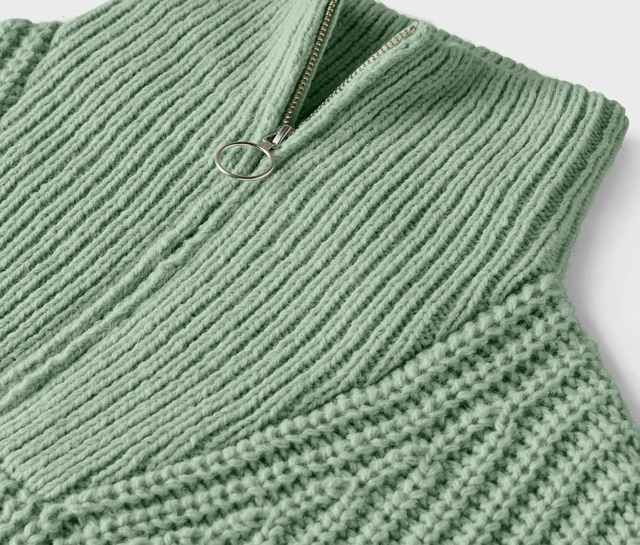 Detailaufnahme eines hellgrünen Strickpullovers mit silbernem Reißverschluss.
