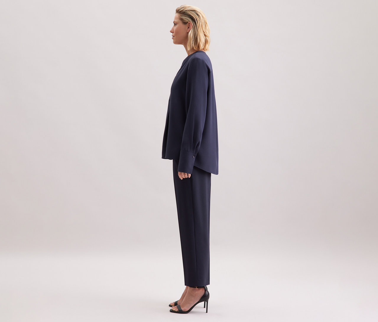 Frau steht seitlich, trägt marineblaue Seidensticker Tunika aus Viskose, Hose und schwarze Sandaletten.