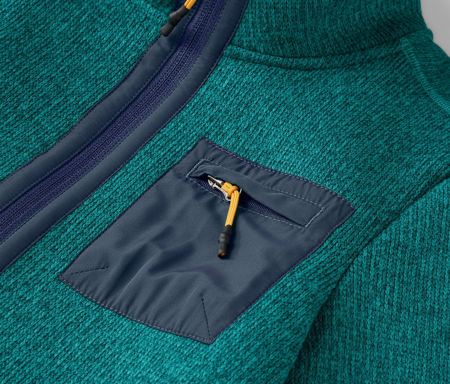 Detailaufnahme eines blaugrünen Fleecepullovers mit Reißverschlusstasche auf der Brust.