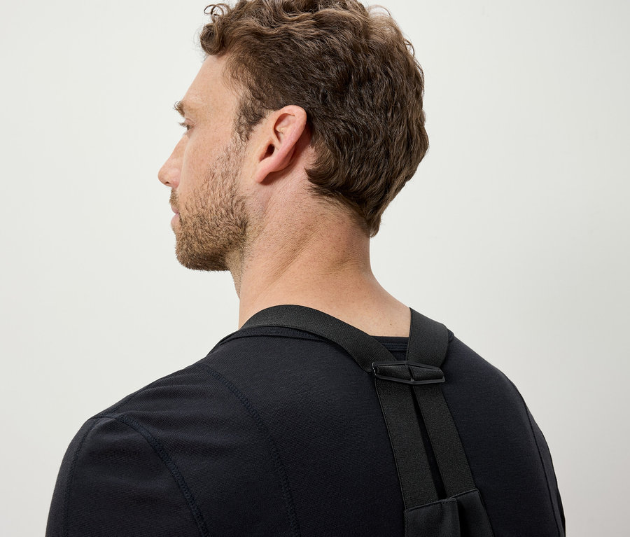 Mann mit braunem Haar trägt ein schwarzes T-Shirt und schwarze Träger.