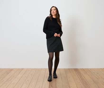 Frau posiert in schwarzem Pullover, gepunktetem Rock, schwarzen Strumpfhosen und Schuhen.