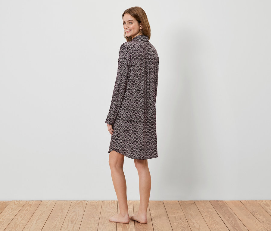 Frau im gemusterten Langarm-Nachthemd blickt über die Schulter.