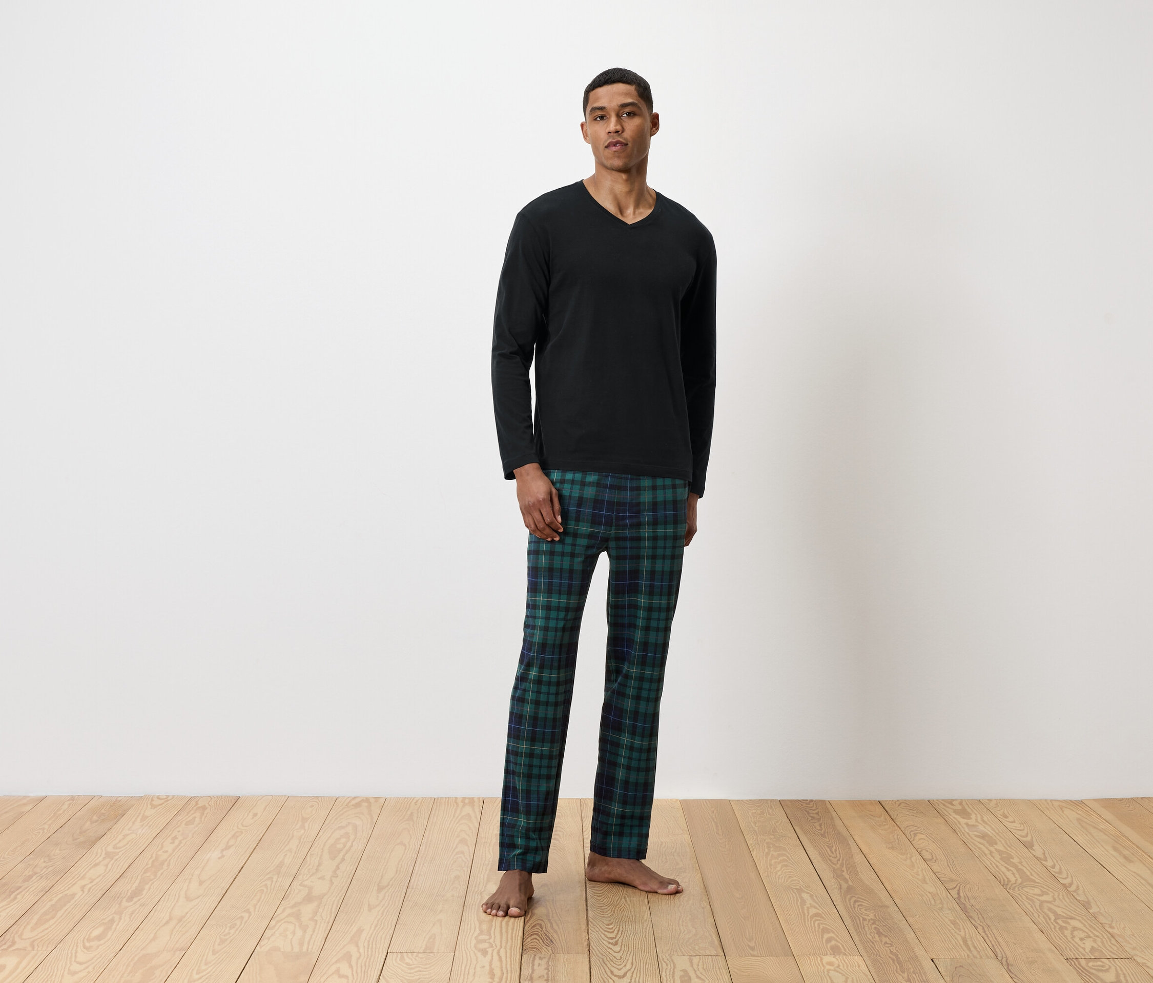 Mann steht in schwarzem Langarmshirt und grün karierter Pyjamahose.