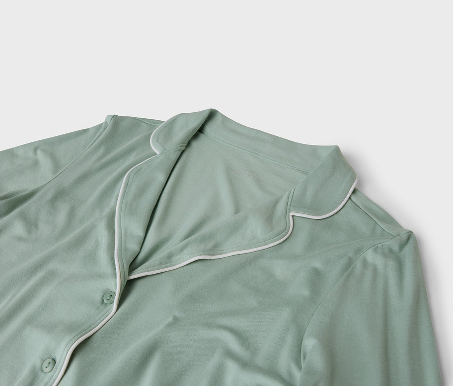 Detailaufnahme eines hellgrünen Pyjamaoberteils mit weißer Paspelierung.