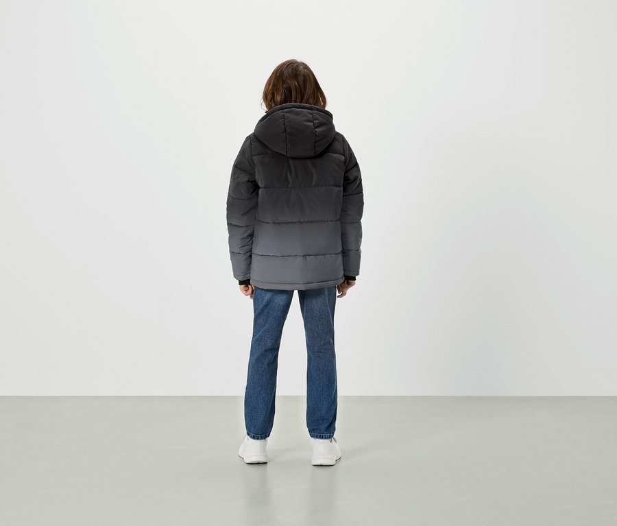 Rückansicht einer Person in grauer Daunenjacke mit Kapuze, blauen Jeans und weißen Schuhen.