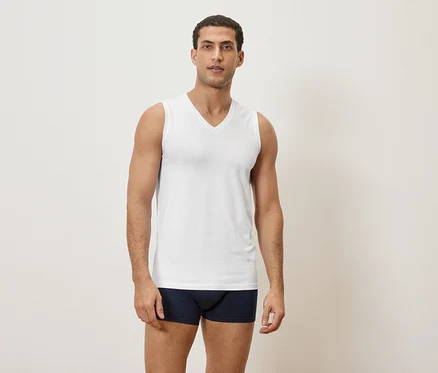 Mann steht in Unterwäsche und weißem Tanktop vor einer schlichten Wand.