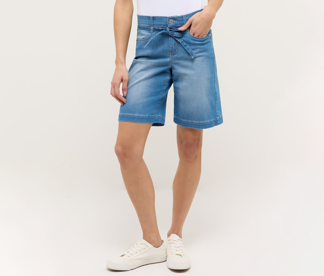 Frau mit hellblauen Angels Denim »Lia City« Shorts und weißen Schuhen, Hand in der Hosentasche.